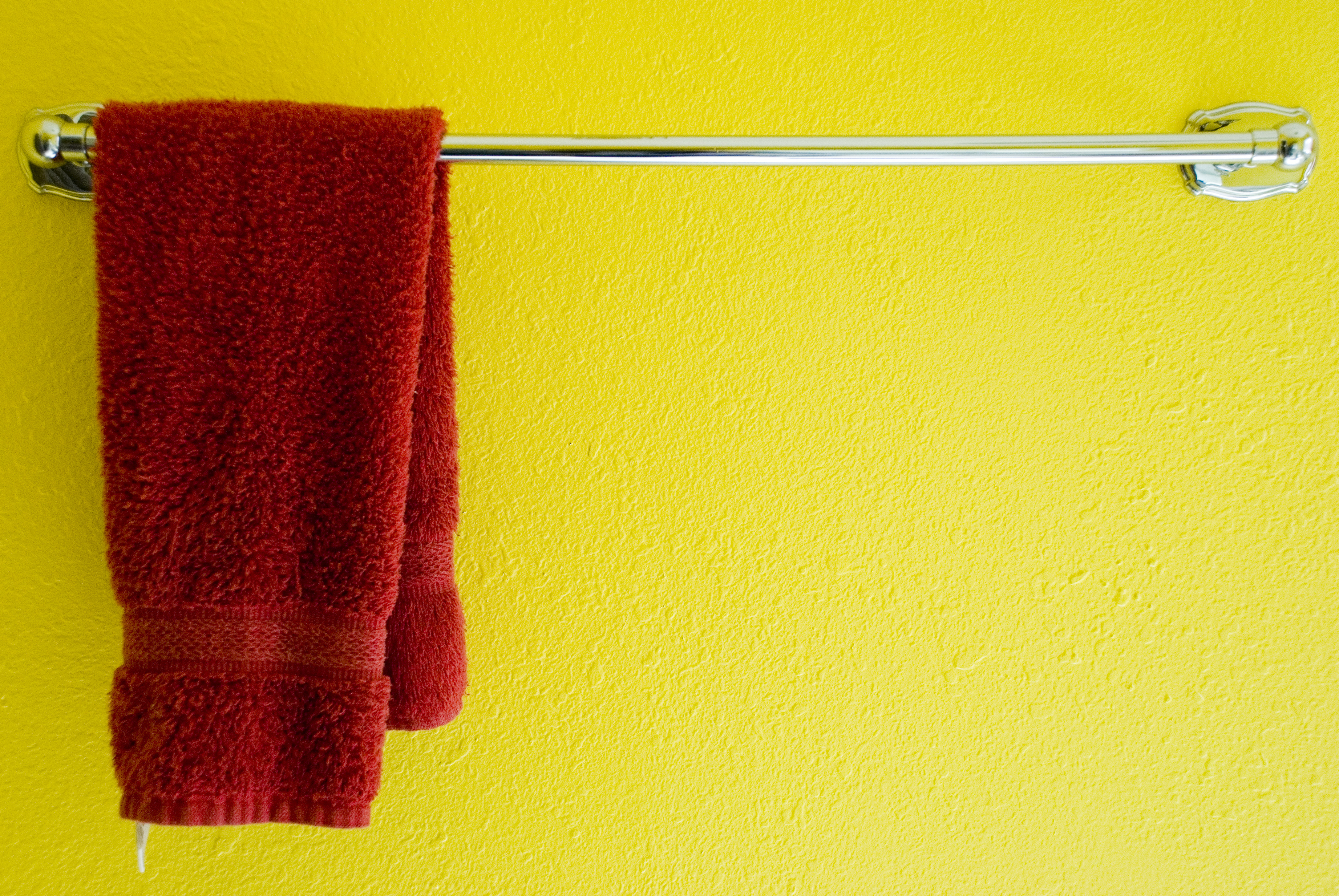 Red towel hanging on towel rack in front of a yellow wall