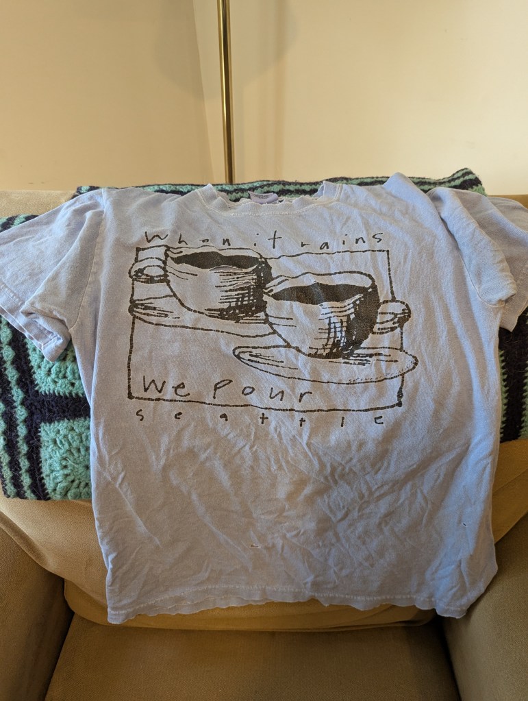 Blue tee shirt with two coffee cups and the words "when it rains, we pour: Seattle